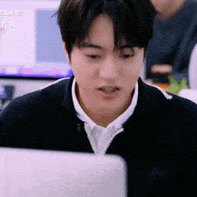 a man in a black sweater is looking at a computer screen with the word sure in the background