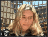 a woman with blonde hair is sitting in a chair with a wicker fence in the background
