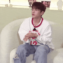 a young man wearing glasses and a white sweatshirt is sitting on a white chair .