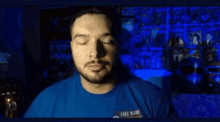 a man with a beard is wearing a blue shirt and looking up in a dark room .