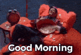 a man is laying in a red chair with a bowl of food and the words good morning written below him