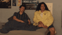 a man and a woman sit on a bed in front of a poster for sous le vent