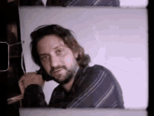 a man with a beard is wearing a plaid shirt and tie and talking on a cell phone .