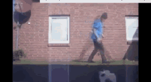 a man in a blue shirt is walking in front of a brick wall