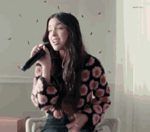 a girl is singing into a microphone while wearing a sweater with flowers on it .