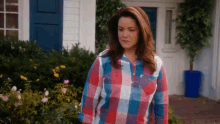 a woman in a plaid shirt is standing in front of a white house