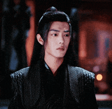 a young man with long hair and a ponytail is wearing a black jacket