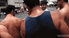 a group of shirtless men are standing on a street with a gifbin.com logo in the corner .