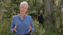 a woman in a blue shirt is standing in the woods with her eyes closed and holding a remote control .