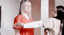 two women are hugging each other in a room . one of the women is wearing an orange scrub top .