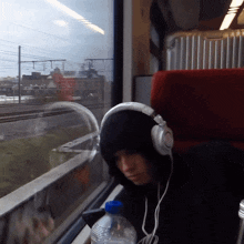 a person wearing headphones sits on a train with a bottle of water