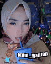 a woman in a hijab drinking from a blue cup with the words emm mantap on the bottom