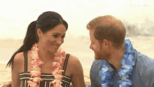 a man and a woman are looking at each other on the beach . the woman is wearing a lei .