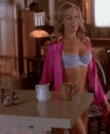 a woman in lingerie is standing in front of a table with a coffee mug on it