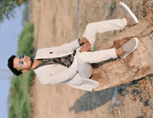 a man in a white suit and sunglasses is sitting on a tree trunk
