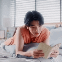 a young man is lying on a bed reading a book .