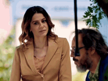a woman in a tan suit is looking at a man with glasses