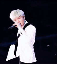 a man in a white suit is singing into a microphone on a stage