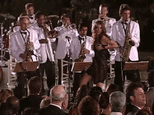 a woman in a black dress is dancing in front of a band playing instruments .