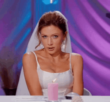 a woman in a wedding dress is sitting at a table with a pink candle on it .
