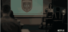 a woman is giving a lecture in front of a projection screen that says lex