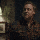 a man in a plaid shirt is sitting in a dark room