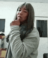 a woman with long hair is standing in a room with her hand on her chin and looking at the camera .
