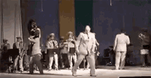 a group of men are dancing on a stage with a band behind them .