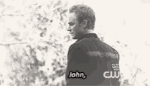 a black and white photo of a man standing in front of trees with the words `` john '' written on his back .