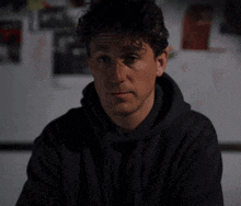 a man with curly hair wearing a black hoodie smiles for the camera
