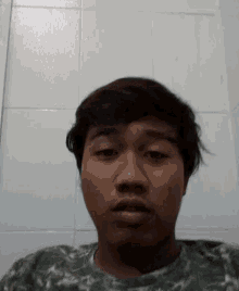 a young man with short hair is making a funny face in front of a white tiled wall .