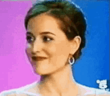 a woman wearing hoop earrings is smiling in front of a blue and pink background