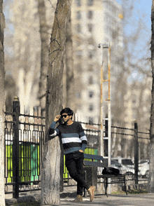 a man leans against a tree while talking on his phone