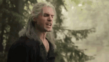 a man with long white hair is standing in a forest .