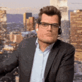 a man wearing glasses and a headset stands in front of a cityscape