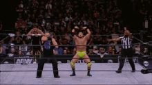 a wrestler in yellow shorts stands in the middle of a wrestling ring with the word aew on the wall behind him