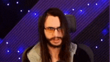 a man with long hair and glasses is making a funny face while sitting in a chair .