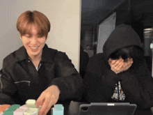 a man in a black hoodie is laughing next to another man in a black hoodie