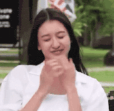 a woman in a white shirt is making a funny face and clapping her hands .