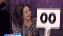 a woman in a plaid shirt is holding a sign that says 00 .