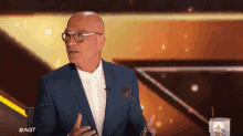 a bald man wearing glasses and a suit is talking into a microphone .