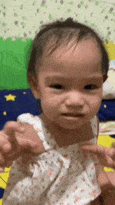 a baby girl in a white dress is making a face