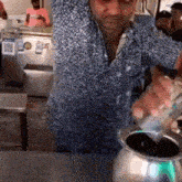 a man in a polka dot shirt is stirring a pot of liquid with a spoon .
