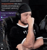 a man wearing headphones and a headband is sitting in a chair with his hand on his nose .