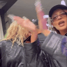 a woman wearing sunglasses and a hat is standing next to another woman wearing a leather jacket