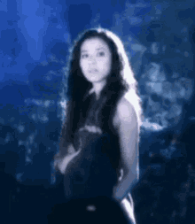 a woman with long black hair is standing in front of a blue background .
