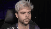 a man with blonde hair and a beard is sitting in a chair and looking at the camera .