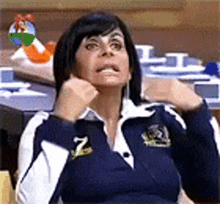 a woman in a blue and white jacket is sitting at a table with her hands on her face .