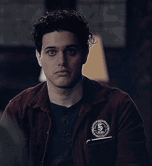 a young man wearing a red jacket and a black shirt is sitting in a dark room .