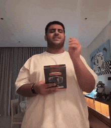 a man in a white t-shirt holds a box of cigarettes